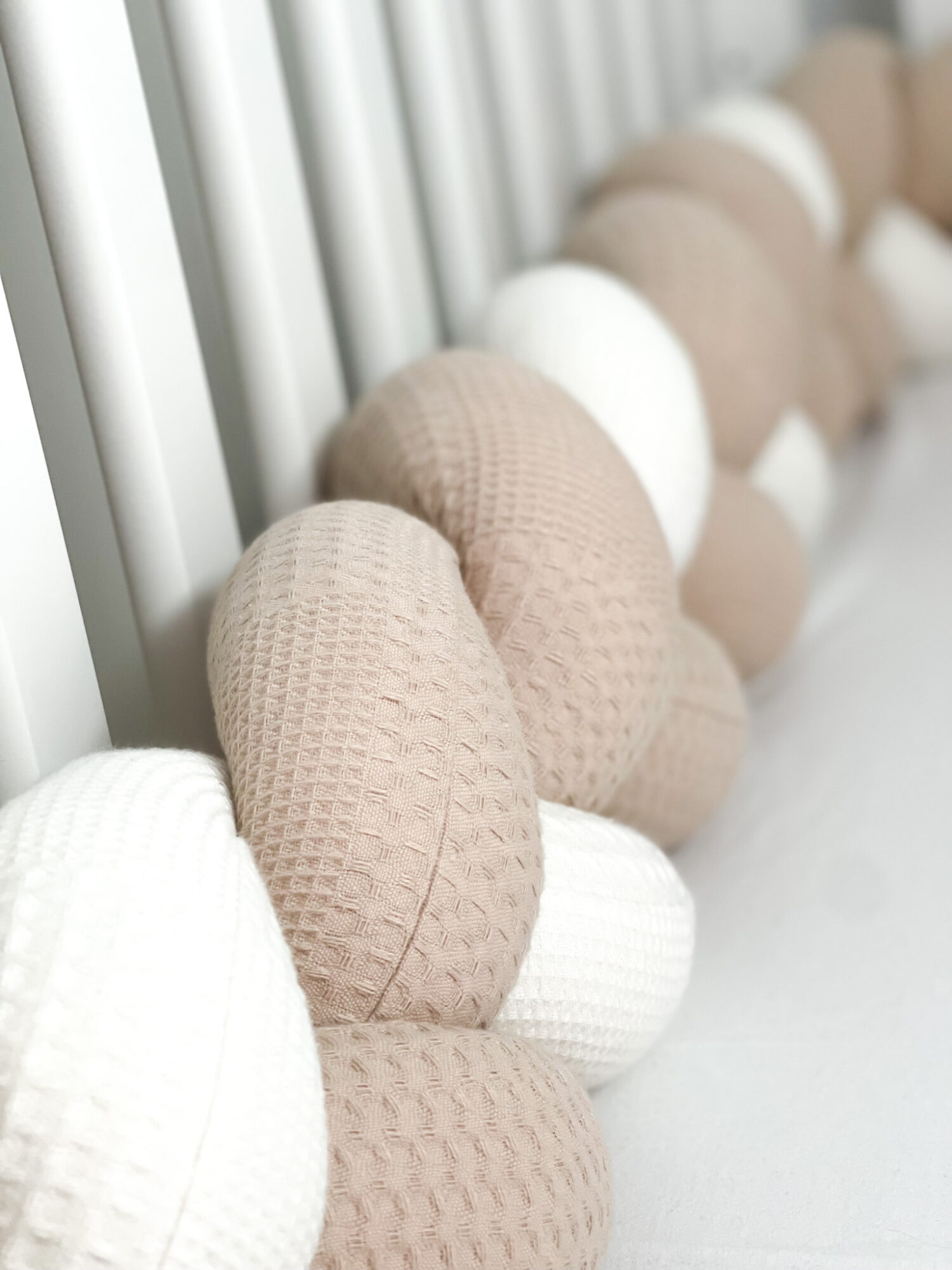 Beige and white Braided Bed Bumper with waffle pattern on display in a baby bed