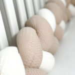 Beige and white Braided Bed Bumper with waffle pattern on display in a baby bed